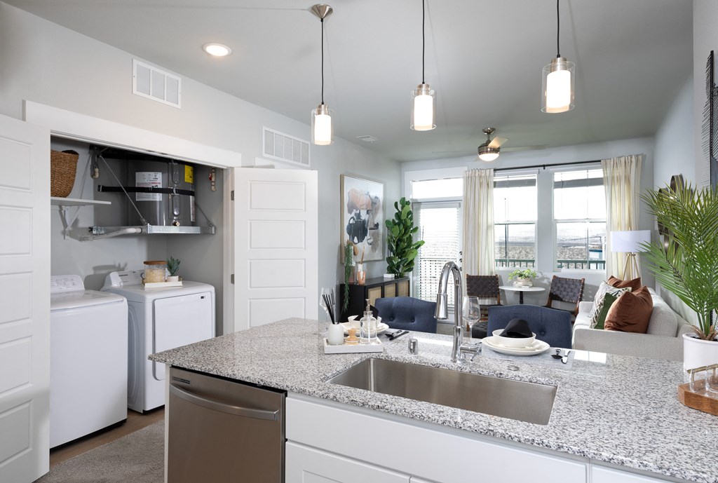 a kitchen opening up to a living room and a closet with laundry machines at a senior apartment community