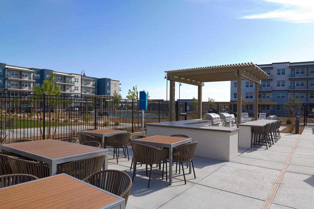 outdoor patio with seating and a grilling station with an island and chairs at a senior apartment community