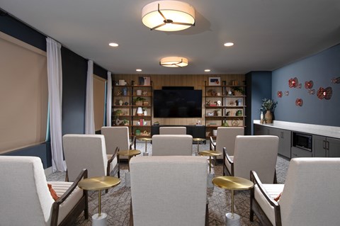 a media room with lounge chairs and large television at a senior apartment community