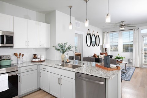 an open kitchen and living room with white cabinets and a granite counter top