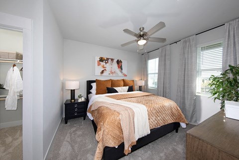 a bedroom with a queen-sized bed, ceiling fan, and windows at a senior apartment community