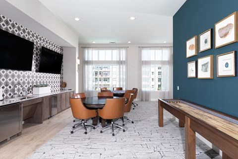 a game room with card tables and chairs, a television, and a table shuffleboard at a senior apartment community