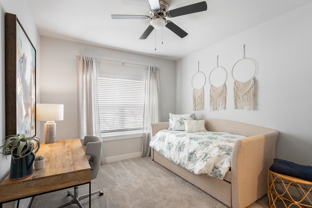 a bedroom with a daybed, desk, ceiling fan, and windows at a senior apartment community