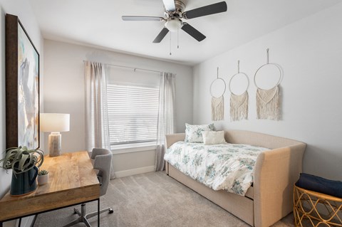 a bedroom with a daybed, desk, ceiling fan, and windows at a senior apartment community