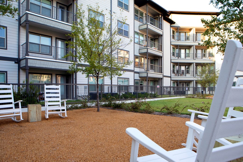 a courtyard with white rocking chairs in front of an apartment building