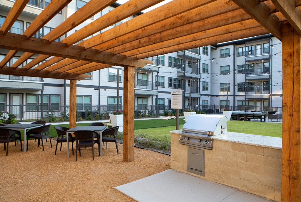 a patio with a grill and tables with chairs in front of an apartment building