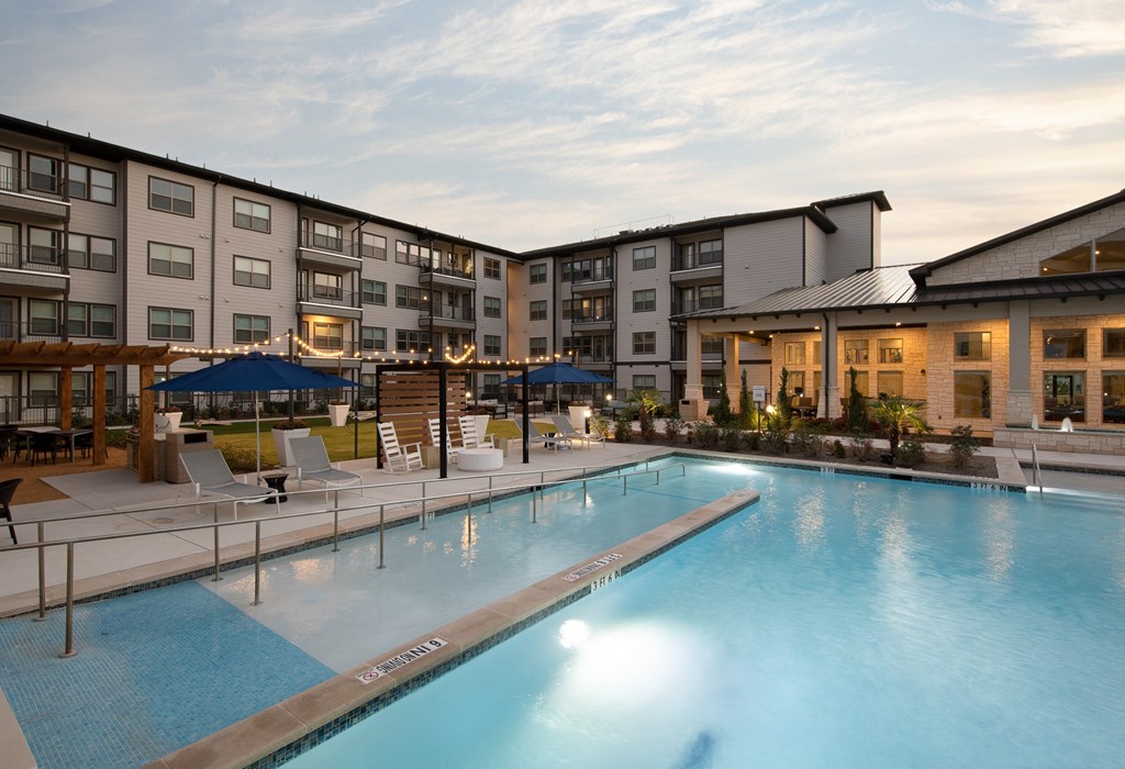 a swimming pool with chairs and umbrellas in front of an apartment building
