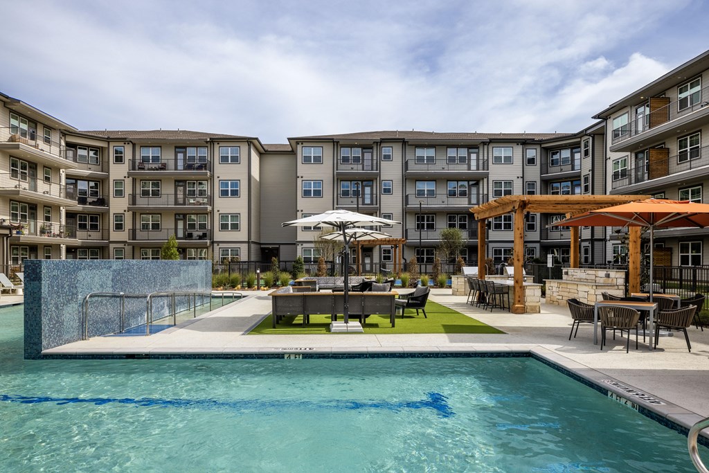 a swimming pool with tables and umbrellas in front of an apartment building