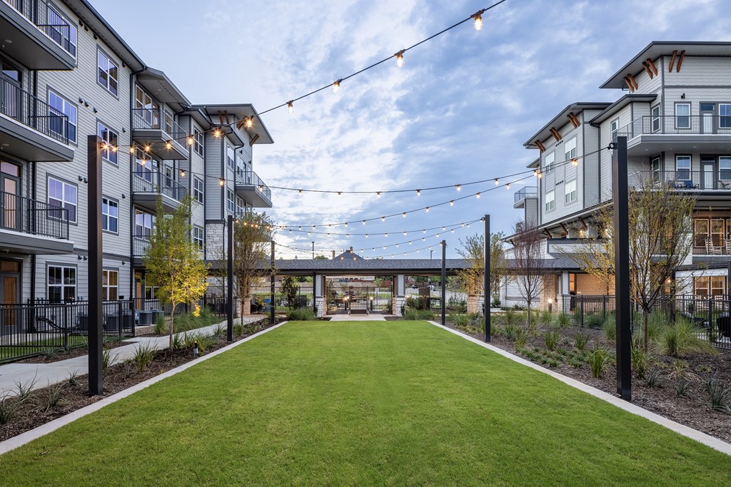 a grassy area with lights hanging over it in front of apartment buildings