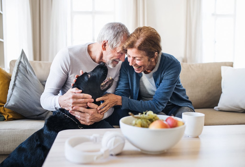 a man and woman sitting on a couch playing with a dog at a senior apartment community