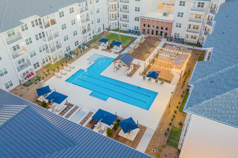 an aerial view of a resort-style pool and lounge areas, lawn, and garden at a senior apartment community