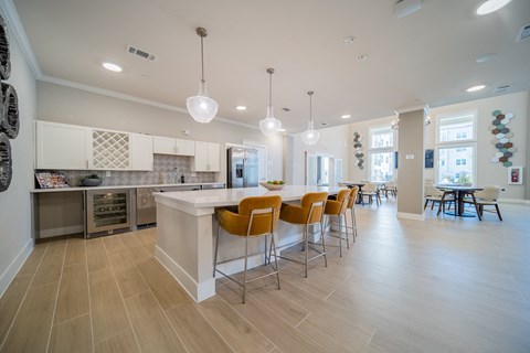 a communal clubhouse kitchen with an island and seating opening up to a dining room at a senior apartment community