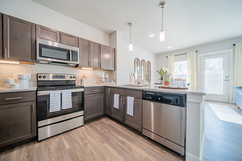 a kitchen with stainless steel appliances and granite countertops opening up to a living room at a senior apartment community