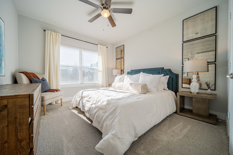 a bedroom with a queen-sized bed, ceiling fan and windows at a senior apartment community