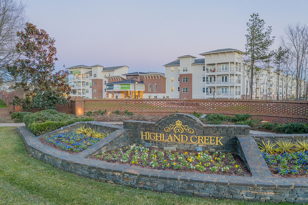 a retaining wall with a sign for highland creek in front of an apartment building