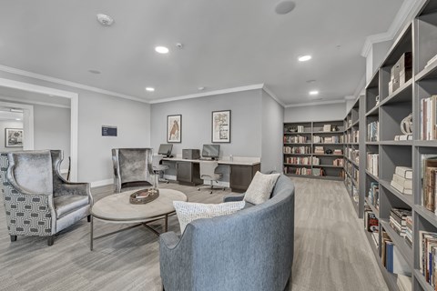 a library with a sitting area and business center with desktops and a printer at a senior apartment community