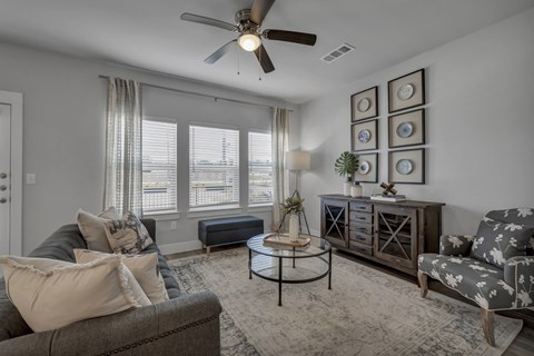 a living room with a ceiling fan and windows at a senior apartment community