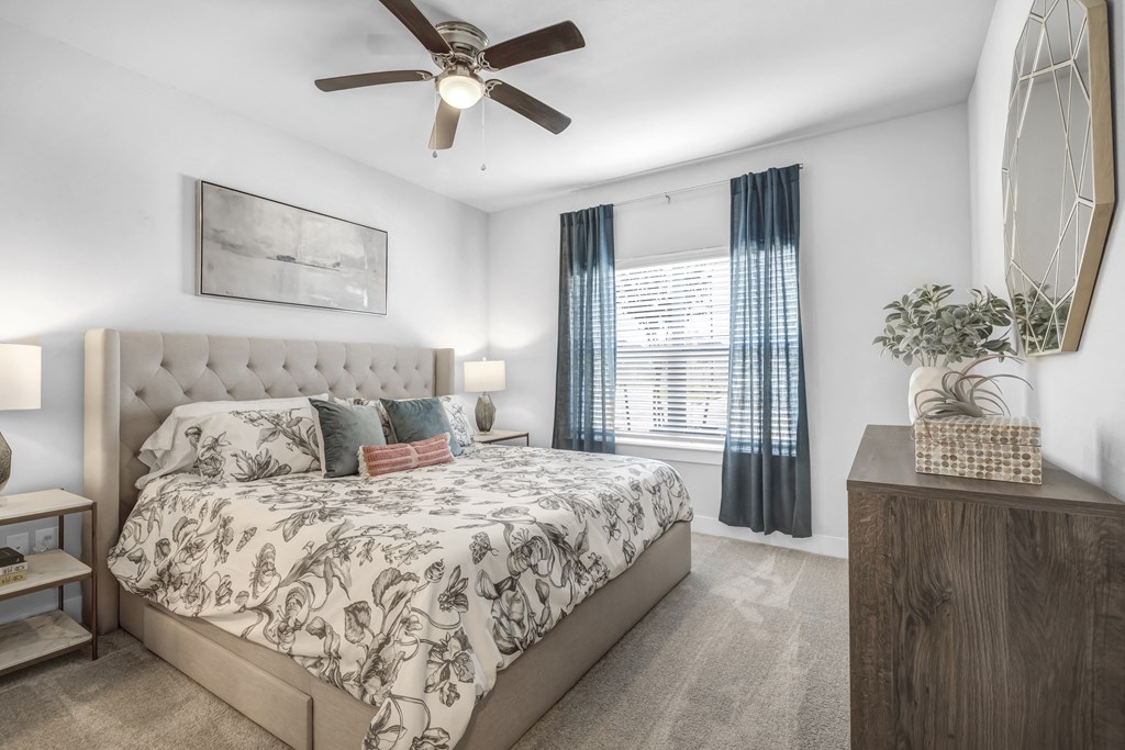 a bedroom with a queen-sized bed, ceiling fan, and windows at a senior apartment community