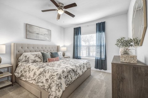 a bedroom with a queen-sized bed, ceiling fan, and windows at a senior apartment community