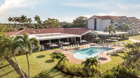 Outdoor pool area with clubhouse and tropical landscaping at The Teale Golden Gate Apartments, Naples, FL
