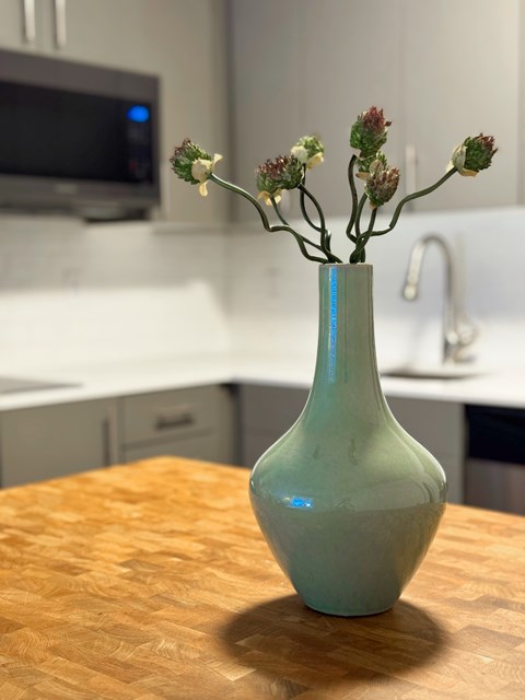 A green vase with flowers on a wooden table in a kitchen.