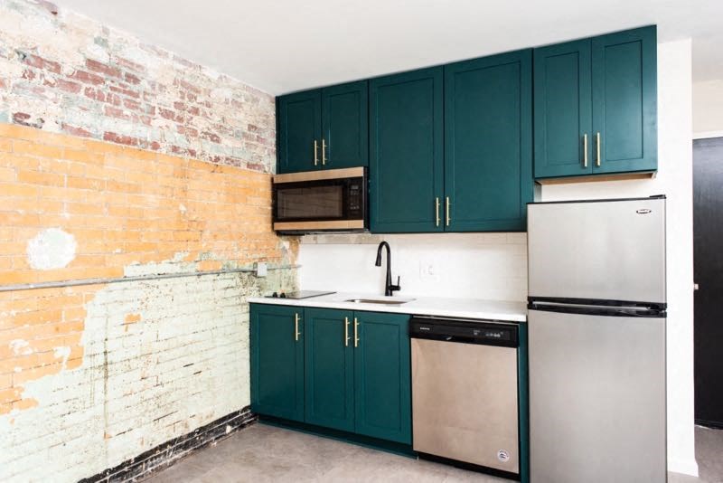 a kitchen with green cabinets and a brick wall