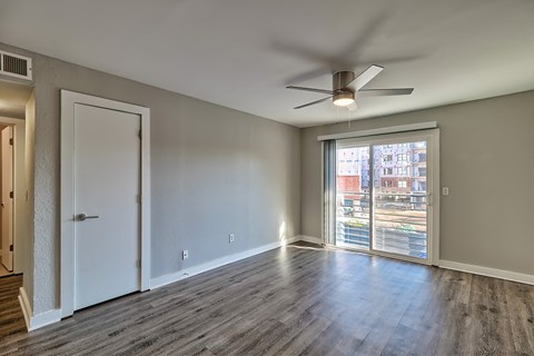 an empty living room with a large window and a ceiling fan