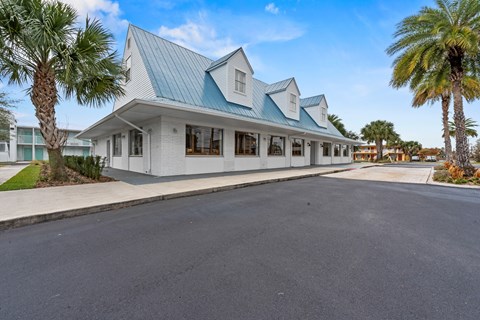 A white building with a blue roof is surrounded by palm trees.at The Teale New Haven Apartments, Melbourne, FL, 32904