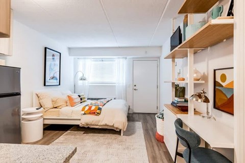 A modern living room with a white sofa and a kitchen area with a refrigerator.