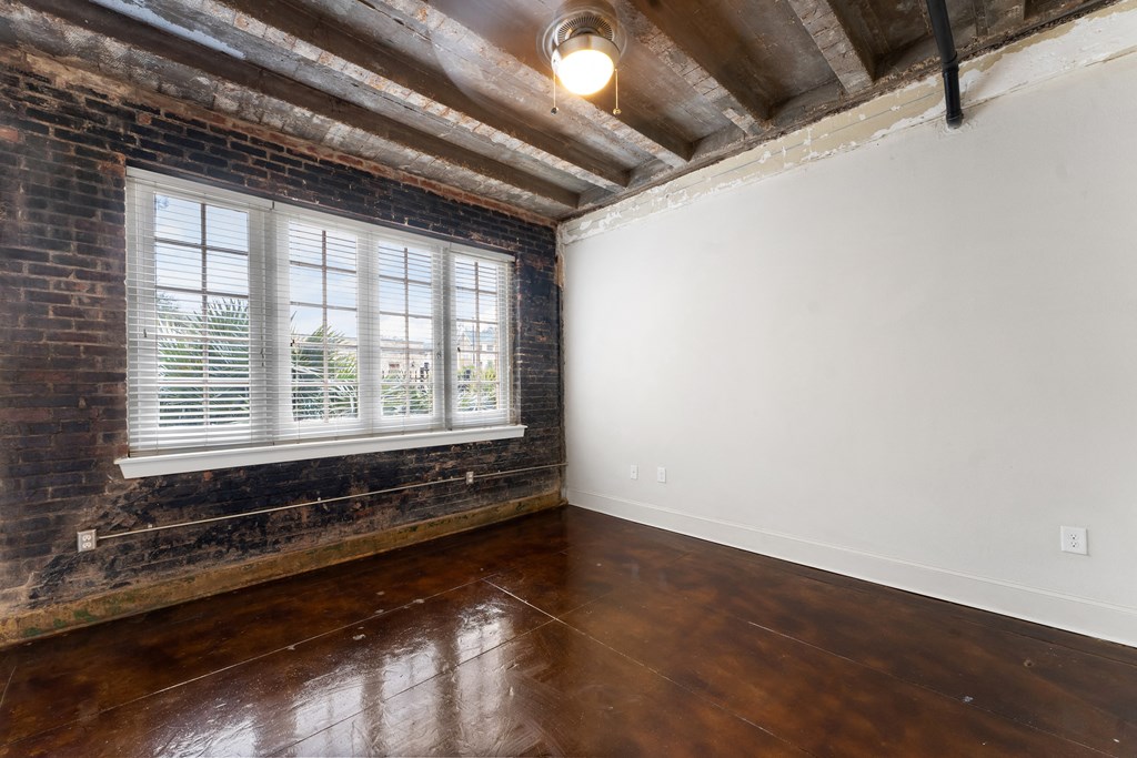 an empty room with wood floors and a brick wall and a window