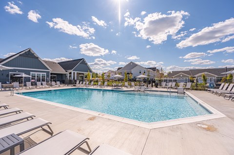 A large outdoor swimming pool surrounded by sun loungers and a building in the background.