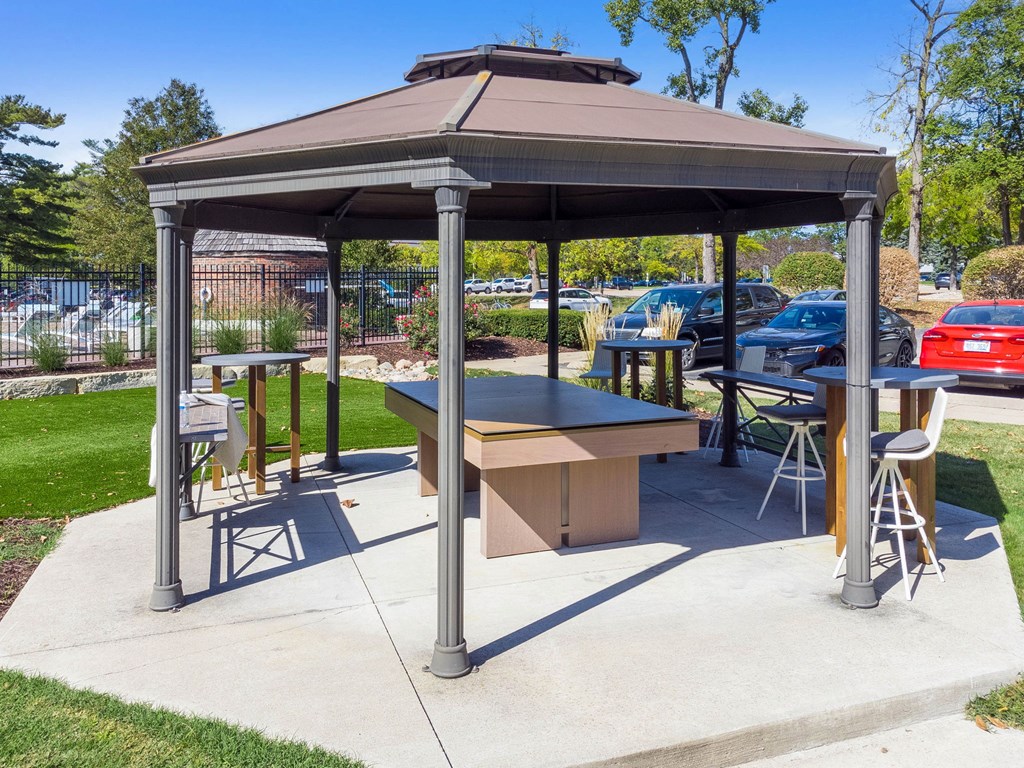A gazebo with a table and chairs is set up in a park.