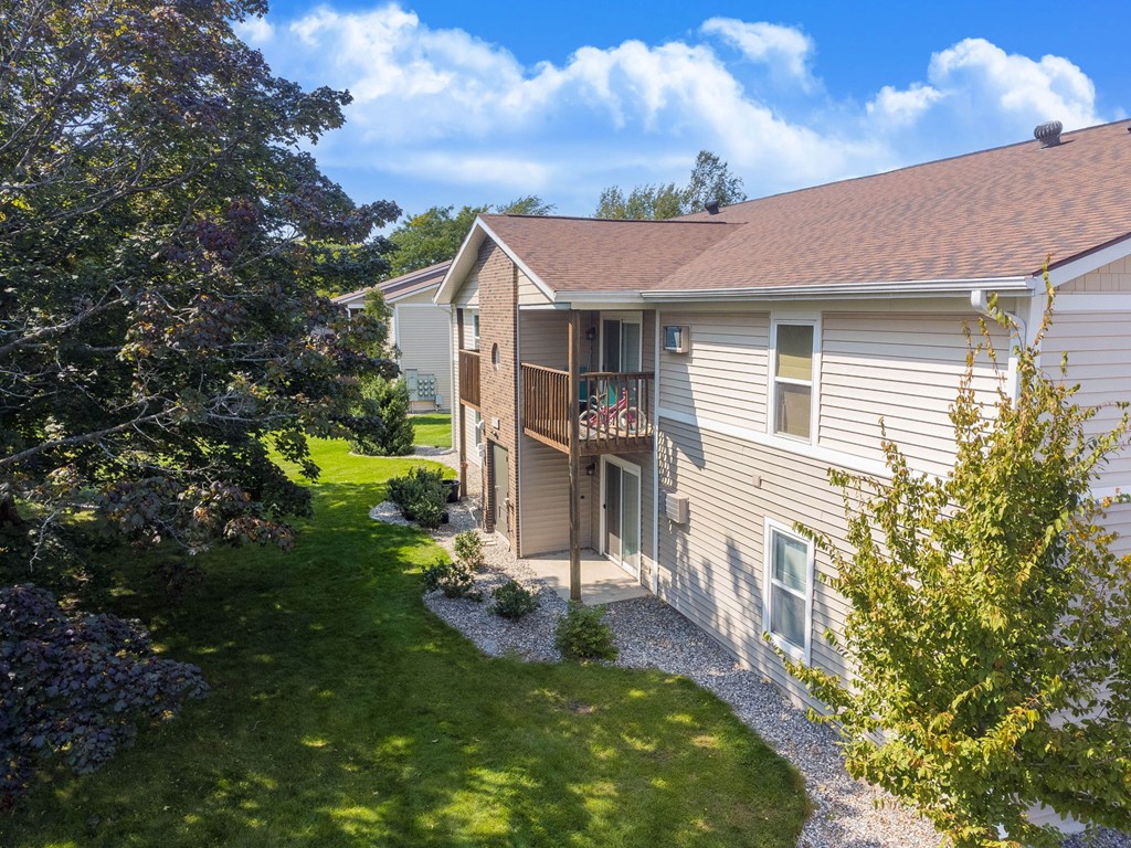 A house with a brown roof and a grey siding is surrounded by a green lawn and trees.
