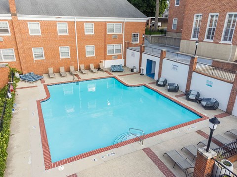 A large swimming pool surrounded by a brick building and lounge chairs.