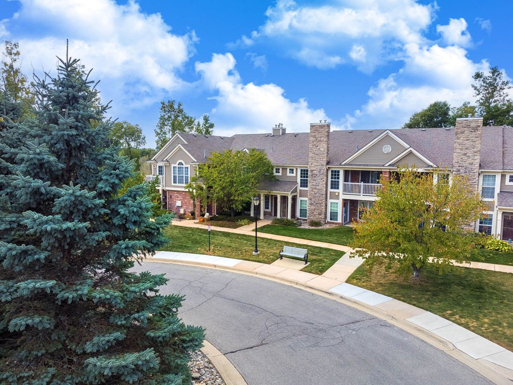 A suburban street with a house and a tree in the foreground.