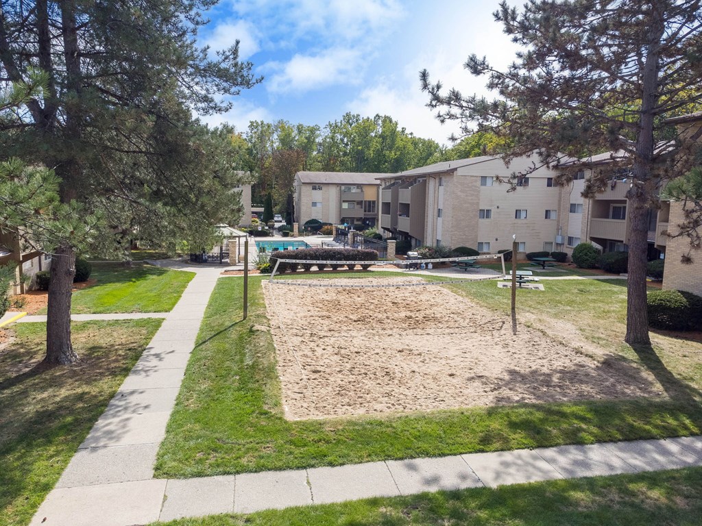 A sandbox in the middle of a grassy area with trees and apartment buildings in the background.