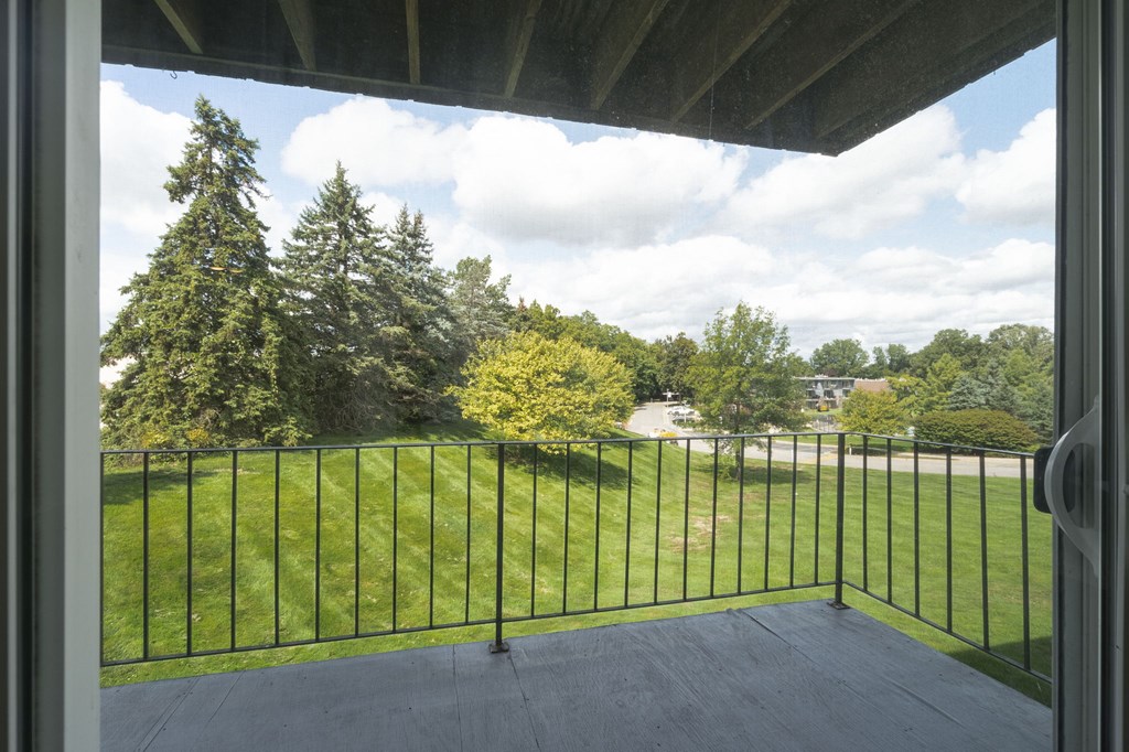 A view from a balcony looking out at a green lawn and trees.