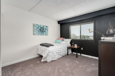 A bedroom with a bed, nightstand, and a window.