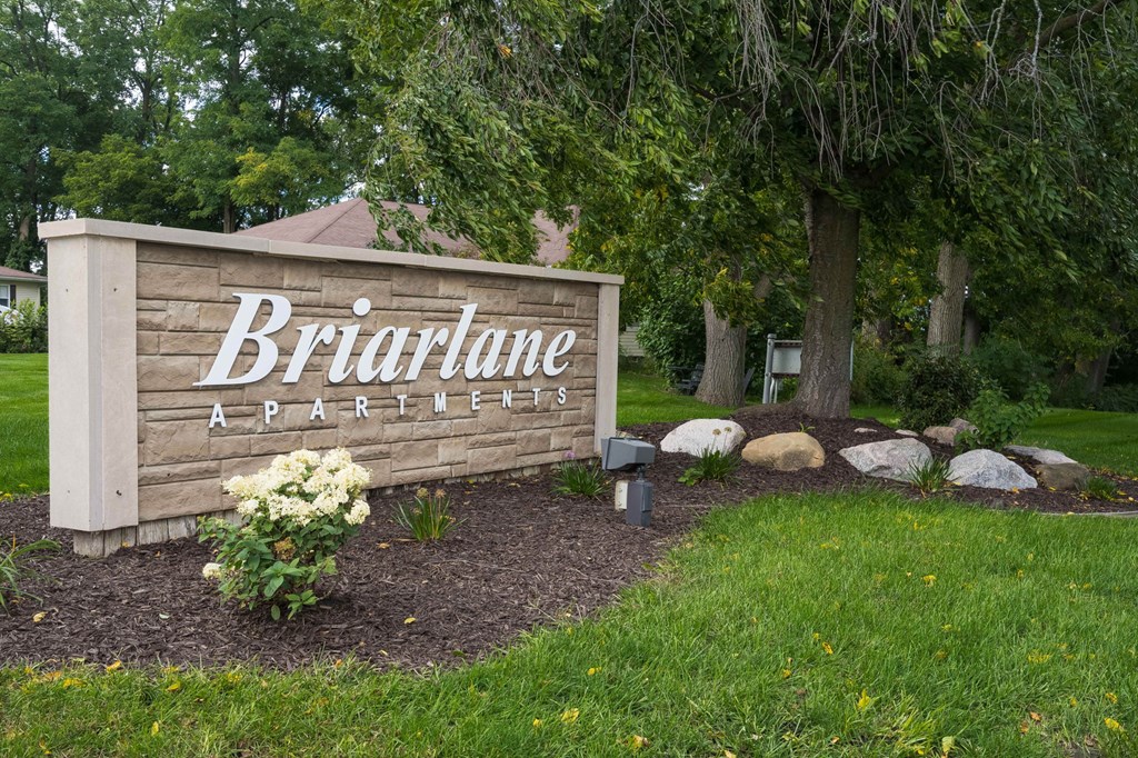 A sign for Briarlane Apartments is surrounded by flowers and trees.