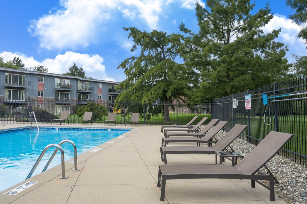 A pool surrounded by trees and chairs.