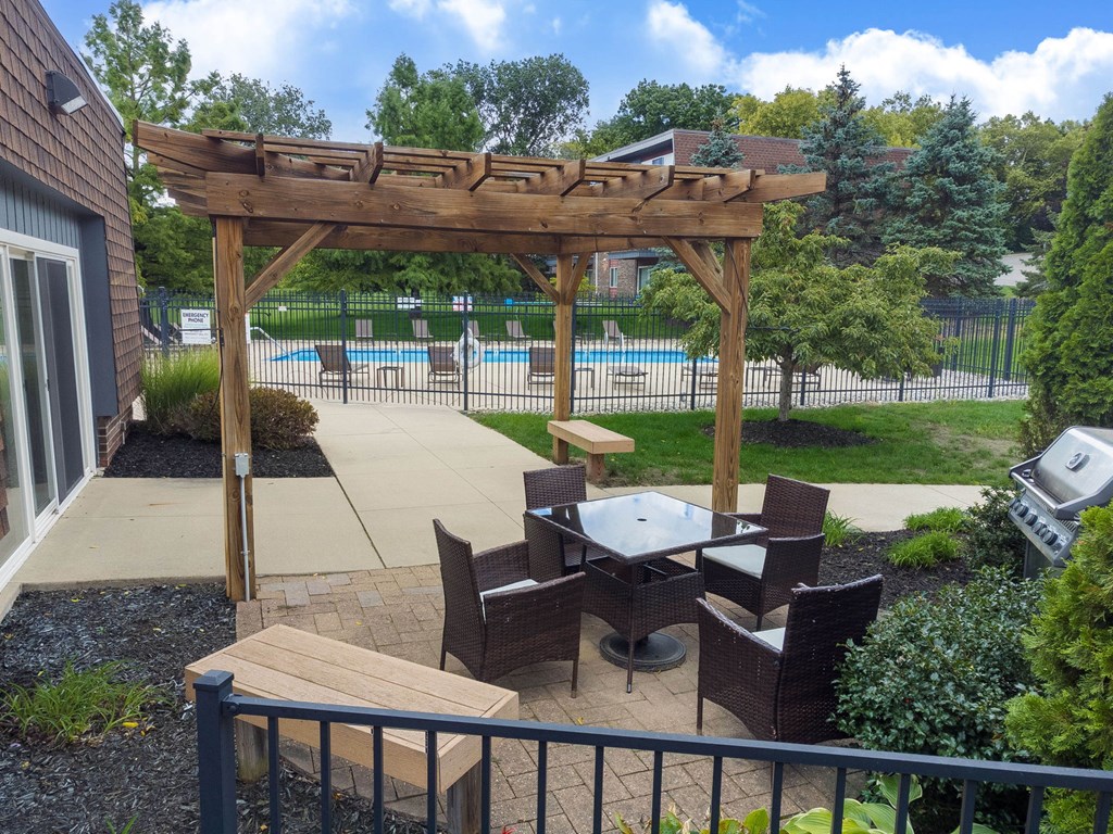 A wooden pergola over a patio table with chairs.