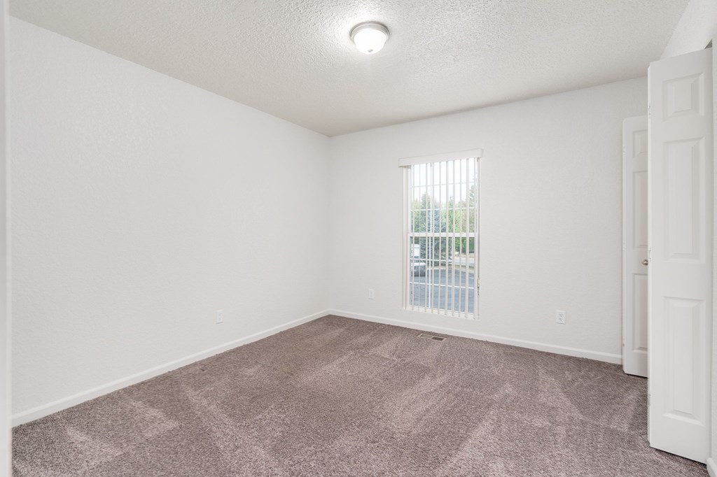 A room with a carpeted floor and a window with blinds.