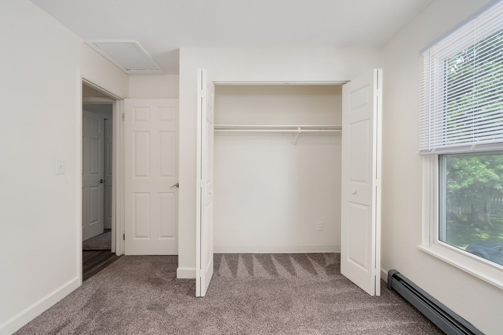 A white closet with a carpeted floor and a window.