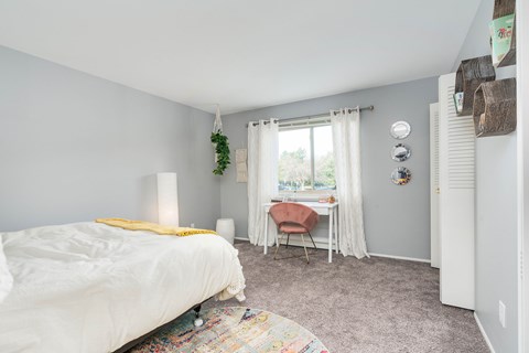 A bedroom with a white bed and a chair by the window.