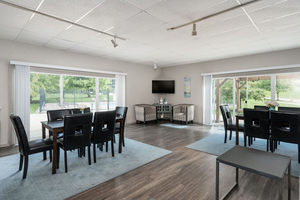 A modern dining room with a TV mounted on the wall and a view of a green lawn outside the window.