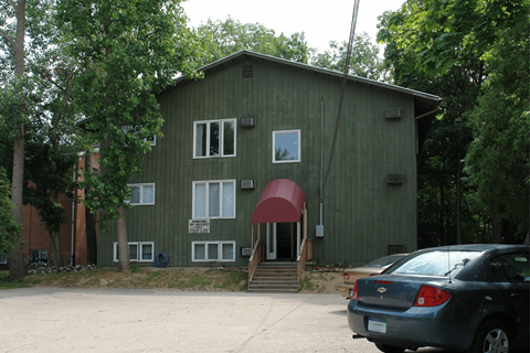 A green building with a red awning and a car parked in front.