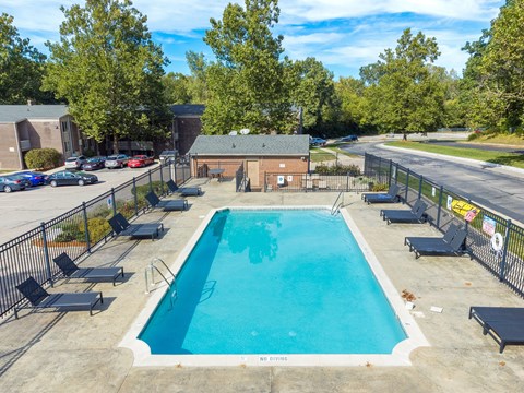 A large outdoor swimming pool surrounded by a fence and lounge chairs.