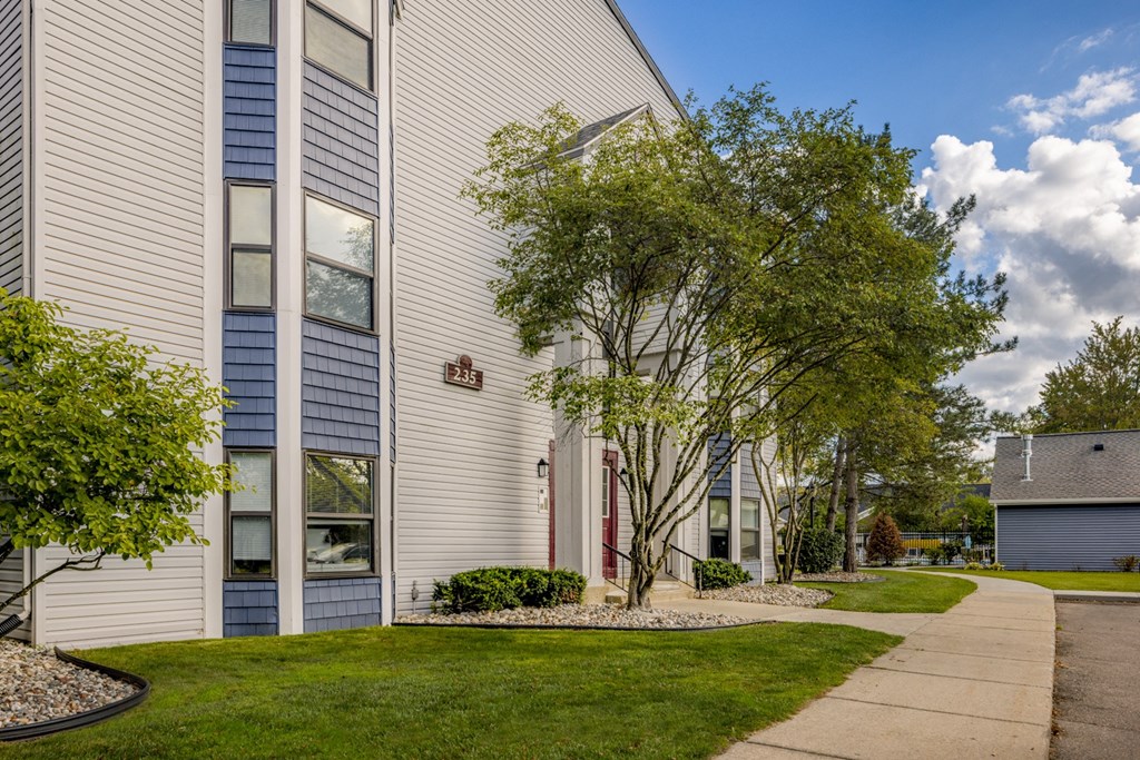 a white building with a sidewalk and trees in front of it