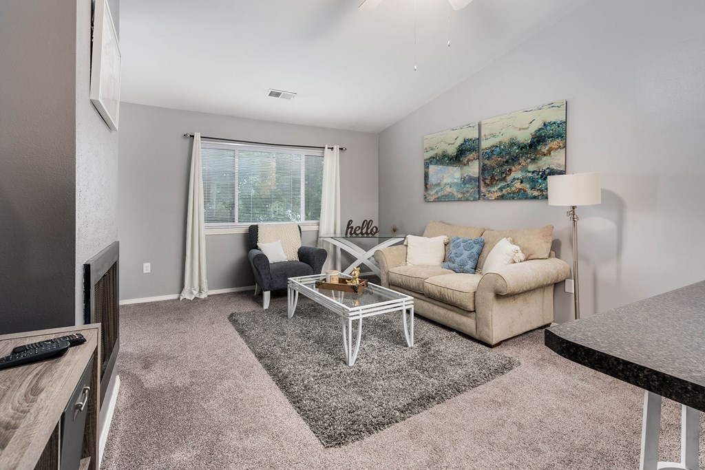 A living room with a grey rug, a white sofa, a glass table, and a painting on the wall.