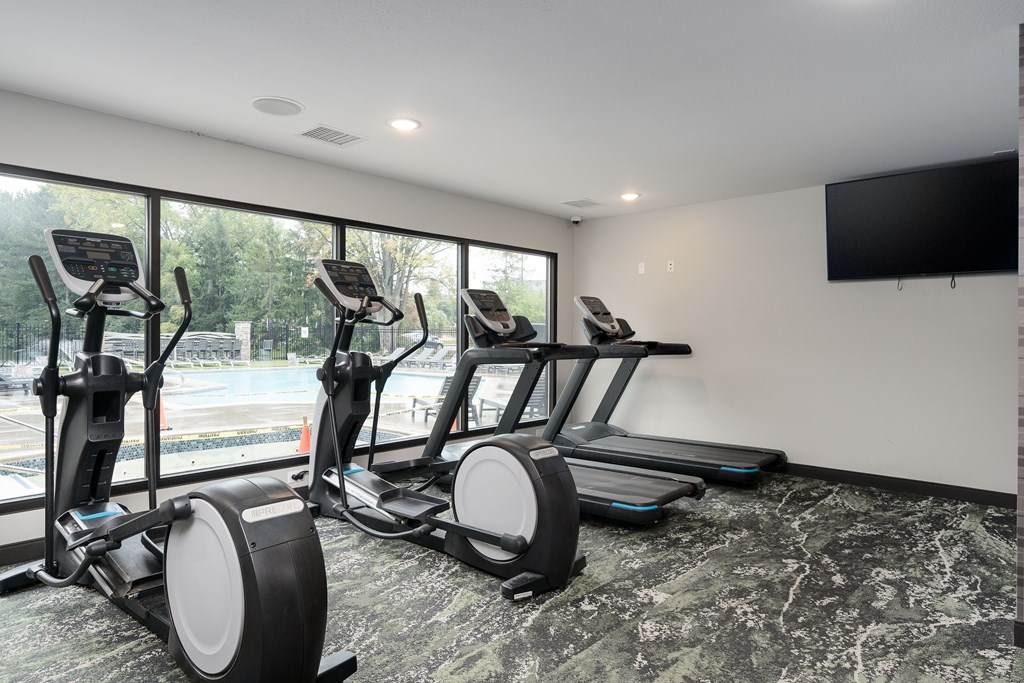 A room with a row of stationary bikes and a television on the wall.